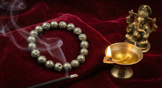 Rustic pyrite bracelet, lit incense stick, brass oil lamp, and Ganesh statue on velvet cloth
