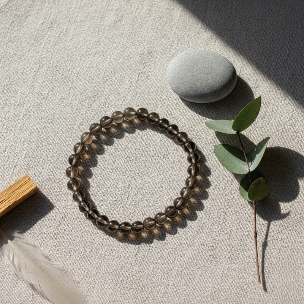 Smoky quartz beaded bracelet on textured fabric with smooth gray stone and eucalyptus branch