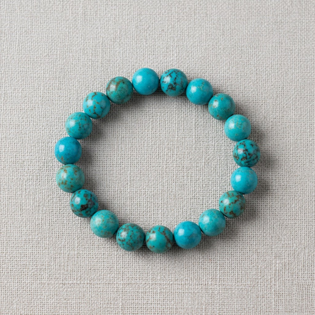 Round turquoise bead bracelet with natural brown veining on beige fabric background