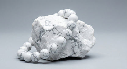 White marble gemstone bead bracelet draped over raw white marble stone on gray background