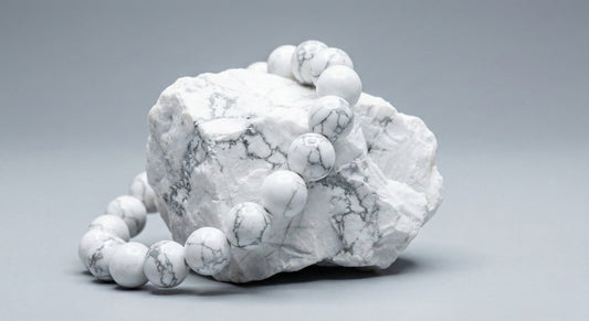 White marble gemstone bead bracelet draped over raw white marble stone on gray background