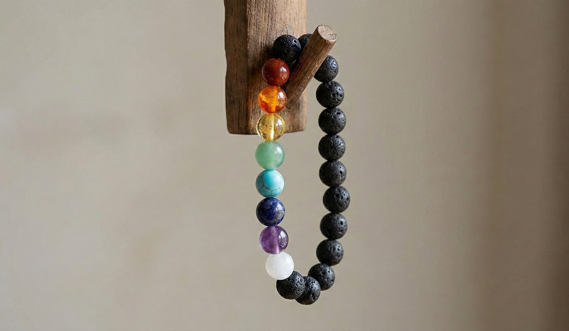 chakra bracelet with multicolored stones and black lava beads hanging on wooden hook