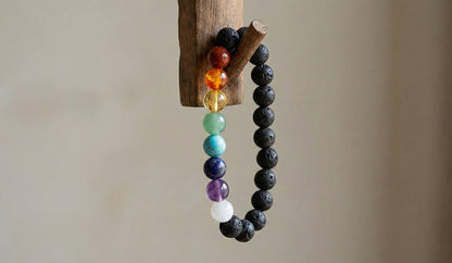 chakra bracelet with multicolored stones and black lava beads hanging on wooden hook