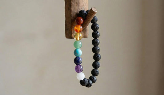 chakra bracelet with multicolored stones and black lava beads hanging on wooden hook