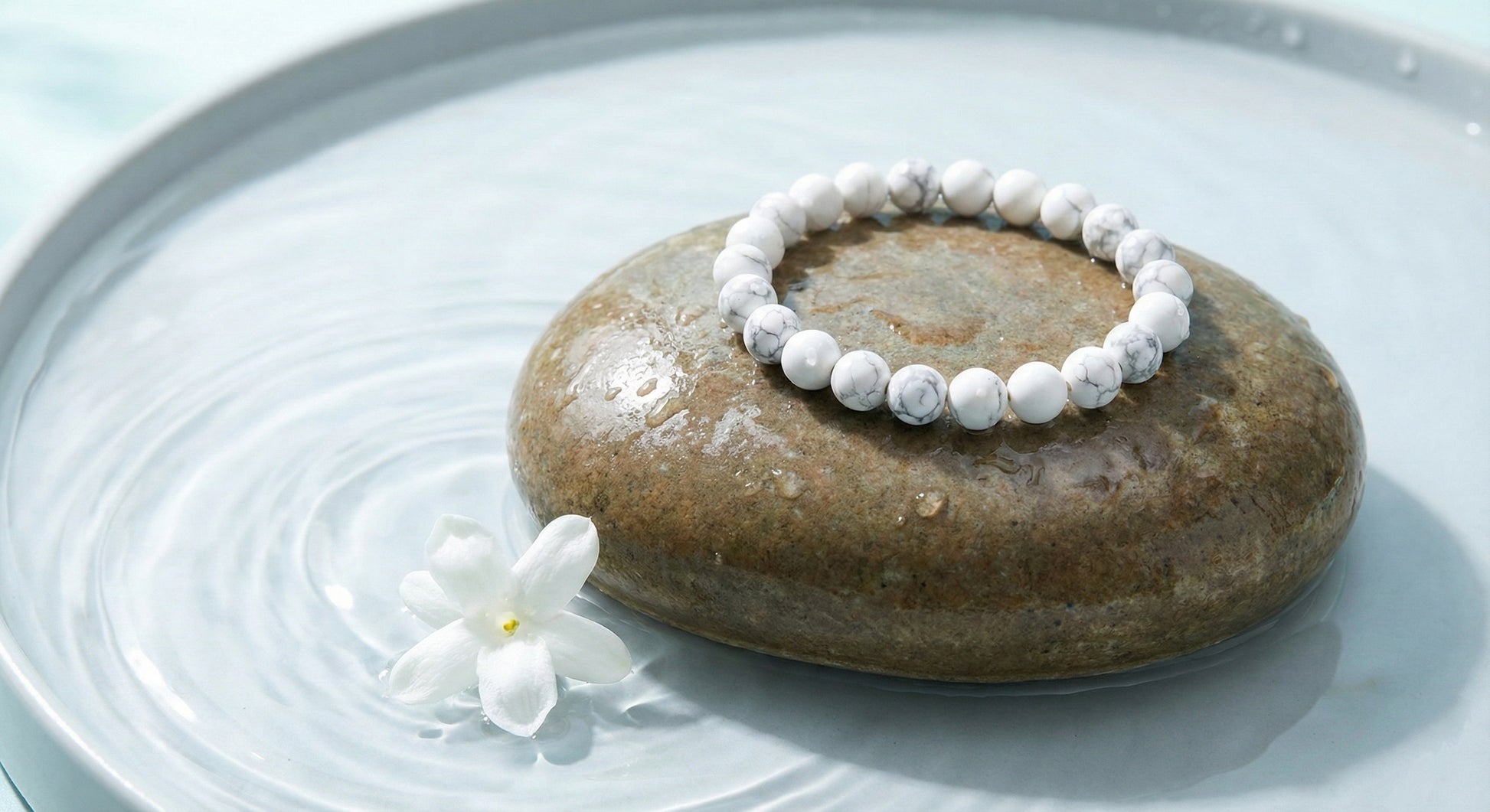 White marble bead bracelet on wet smooth stone with white flower in water bowl for wellness