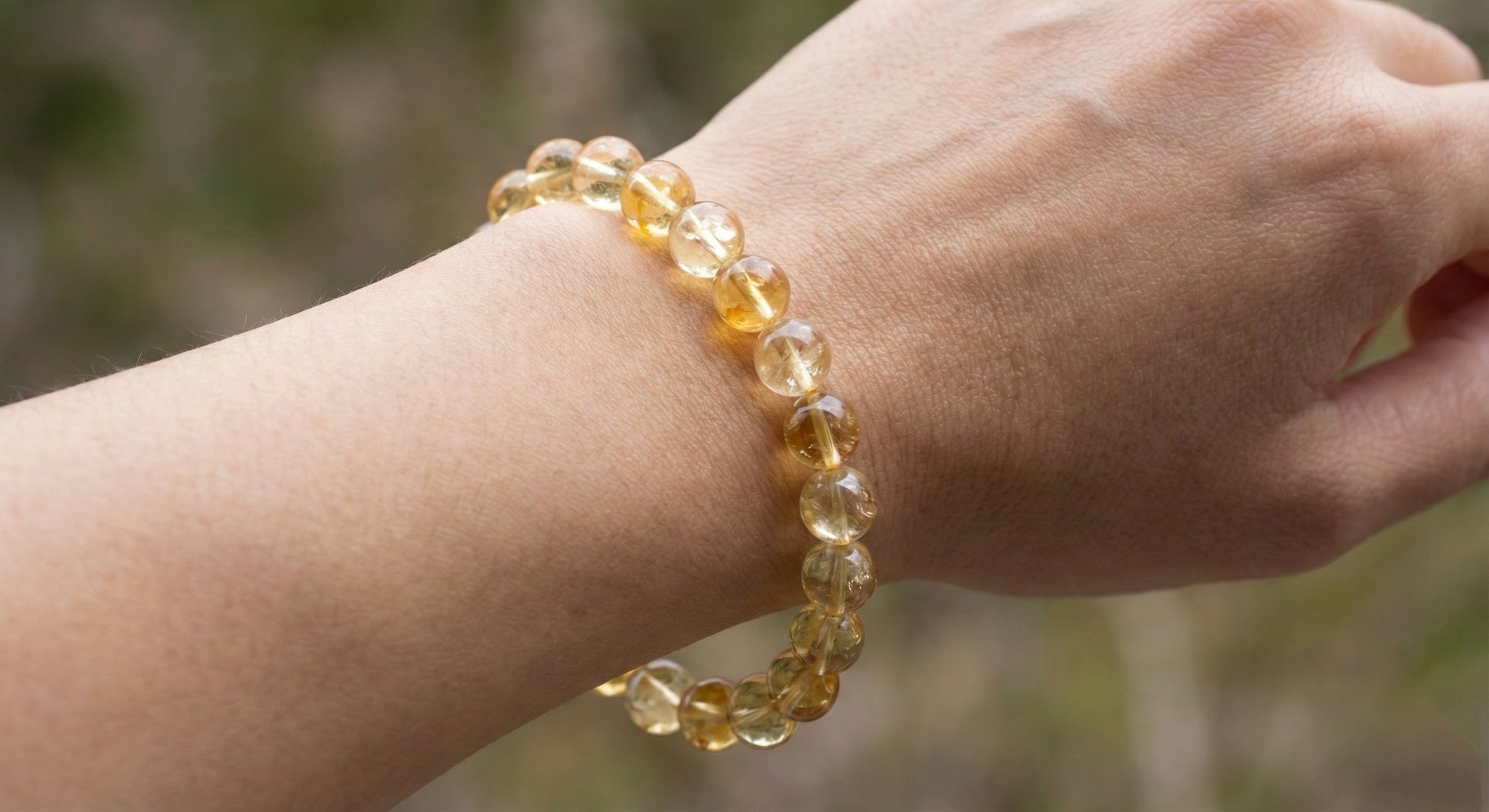 Close-up of wrist wearing a translucent yellow citrine bead bracelet against blurred natural background