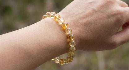 Close-up of wrist wearing a translucent yellow citrine bead bracelet against blurred natural background