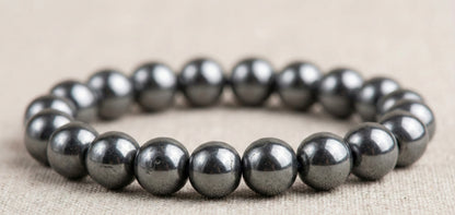 Close-up of a shiny metallic hematite bead bracelet on beige fabric background