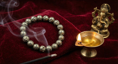 Rustic pyrite bracelet, lit incense stick, brass oil lamp, and Ganesh statue on velvet cloth