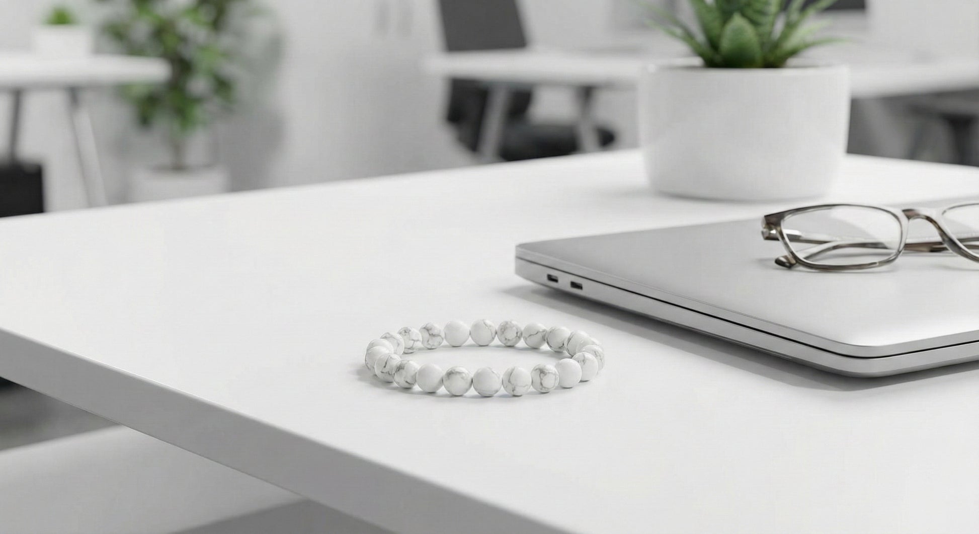 White marble bead bracelet on white office desk beside closed laptop and eyeglasses