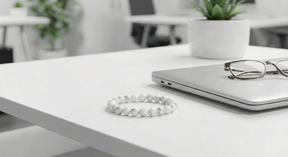 White marble bead bracelet on white office desk beside closed laptop and eyeglasses