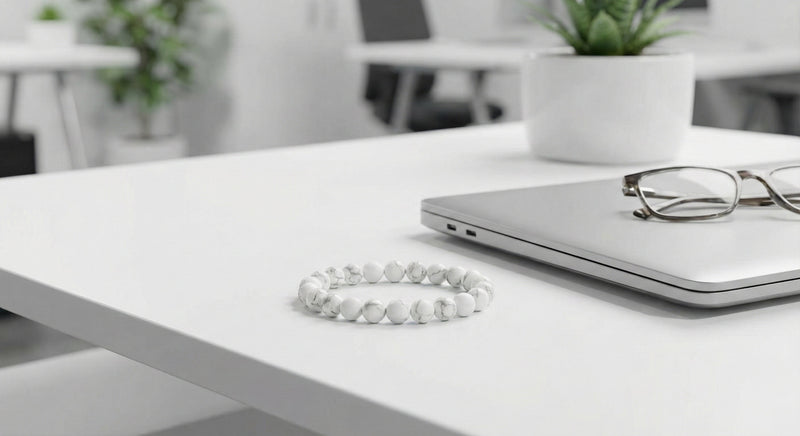 White marble bead bracelet on white office desk beside closed laptop and eyeglasses
