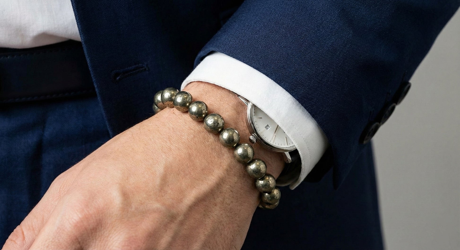 Close-up of wrist with silver beaded bracelet and classic watch under navy suit sleeve