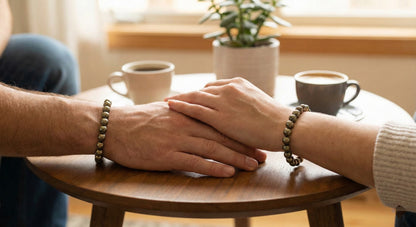 Couple holding hands on wooden table with matching beaded bracelets and coffee cups