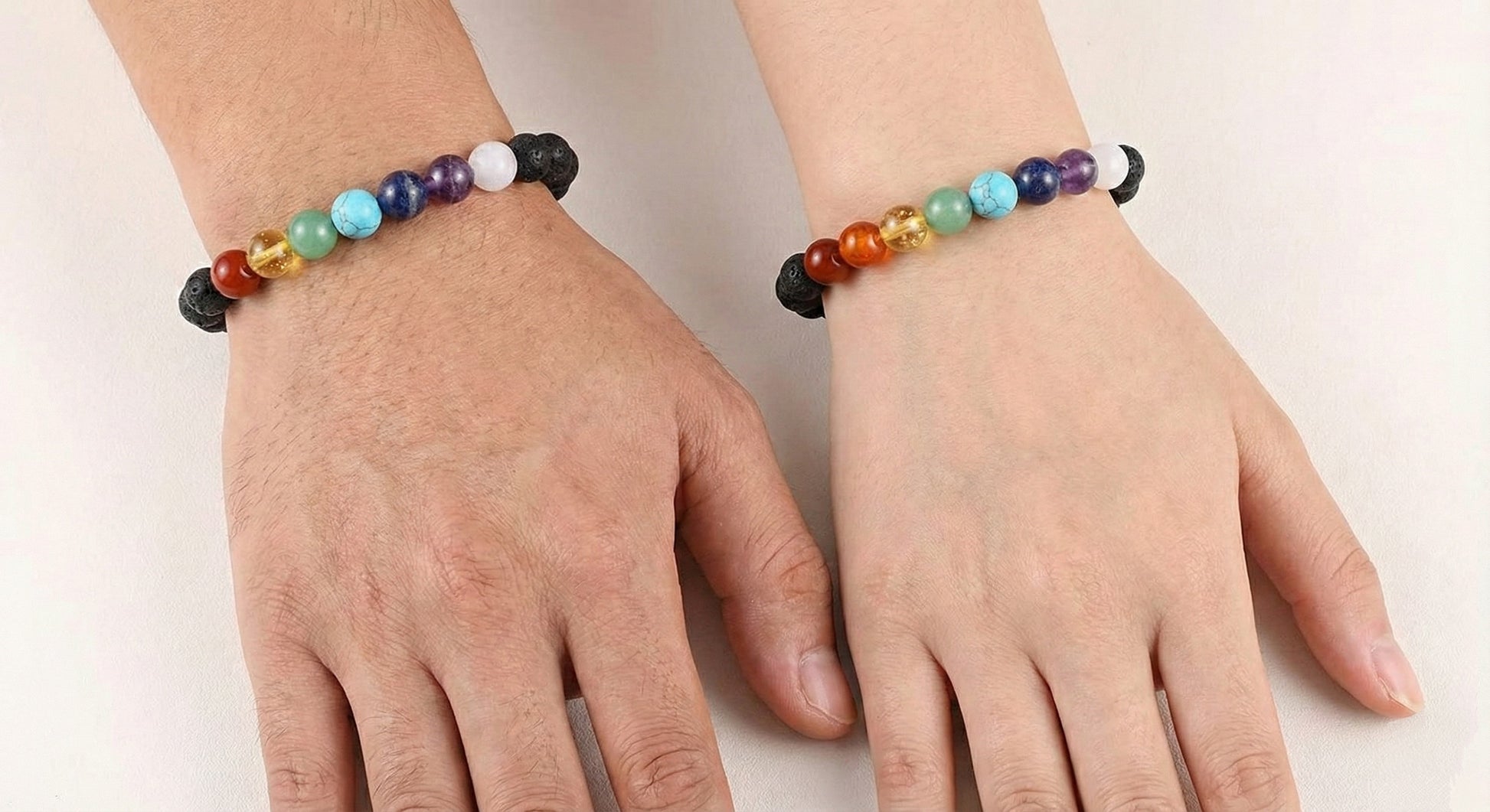Pair of hands wearing matching chakra gemstone beaded bracelets with black lava stones