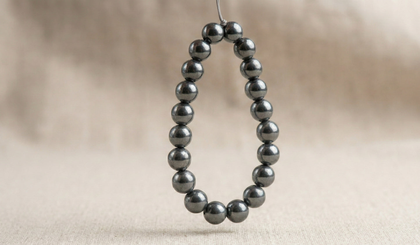 Close-up of a metallic hematite bead bracelet hanging against a neutral beige fabric background