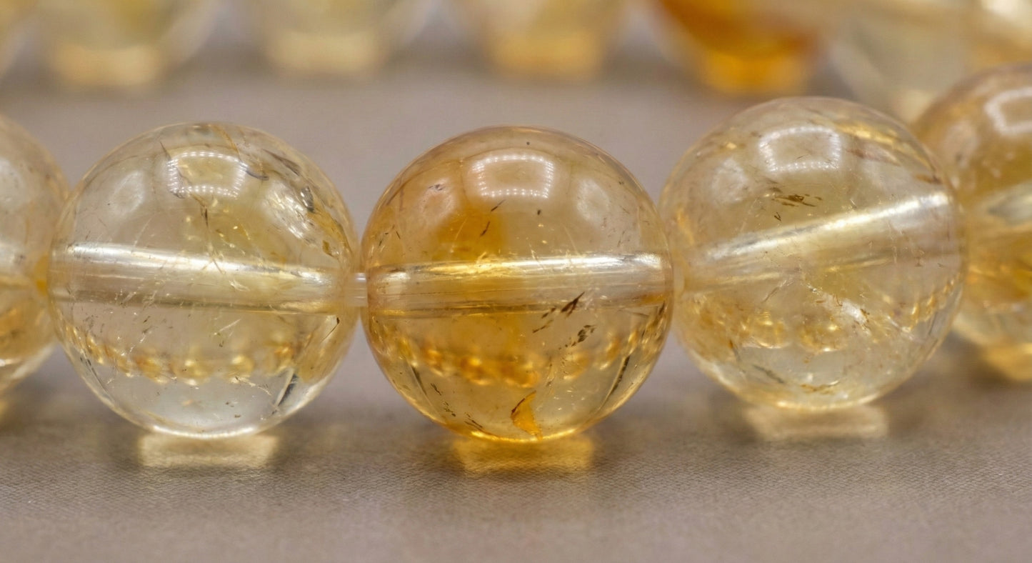 Close-up of polished translucent yellow citrine beads with natural inclusions on a neutral background