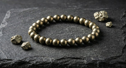 Pyrite beaded bracelet on dark stone surface with raw pyrite mineral chunks