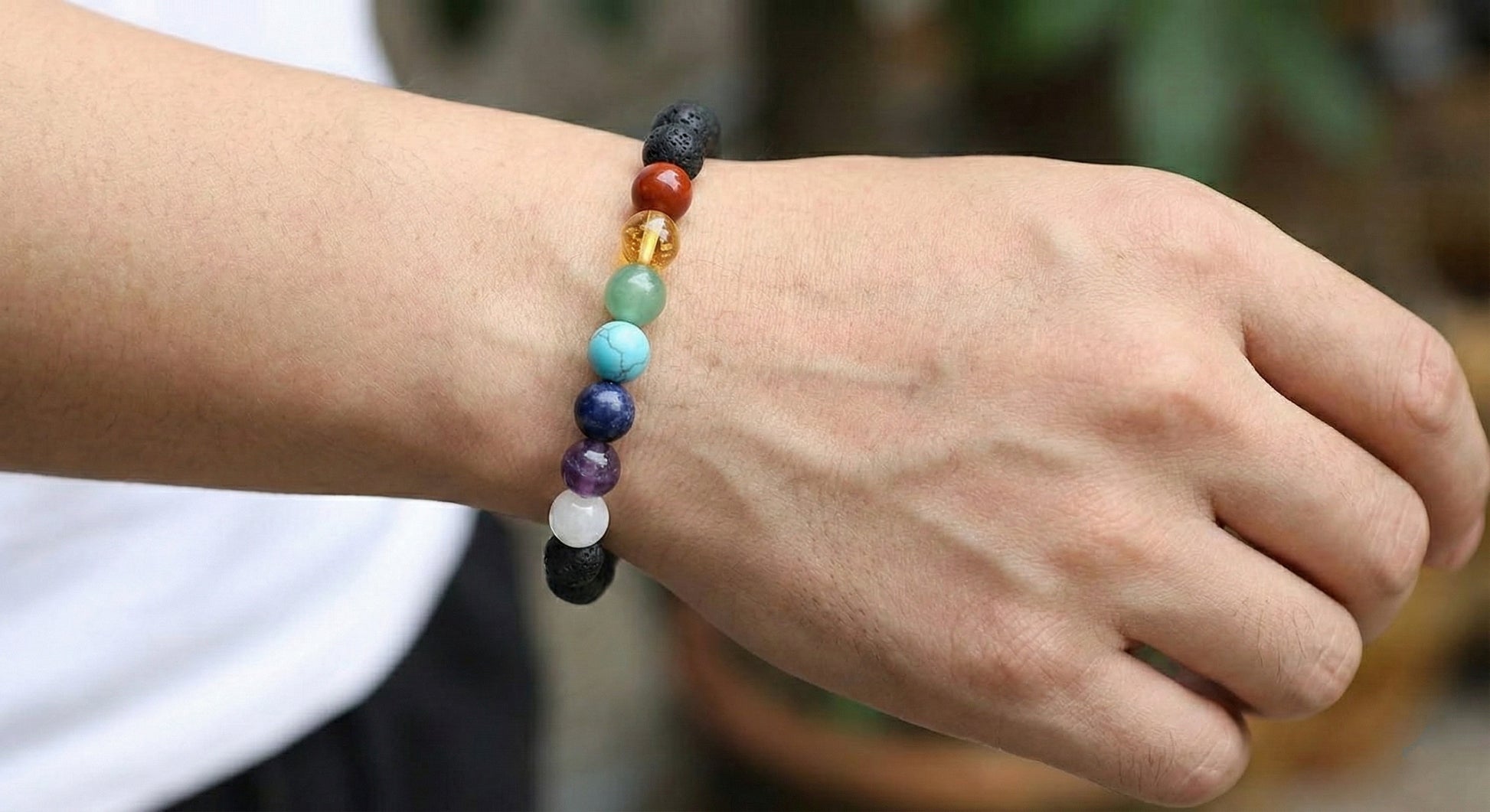 Close-up of hand wearing chakra stone bracelet with colorful round beads and lava stones