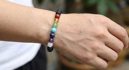 Close-up of hand wearing chakra stone bracelet with colorful round beads and lava stones