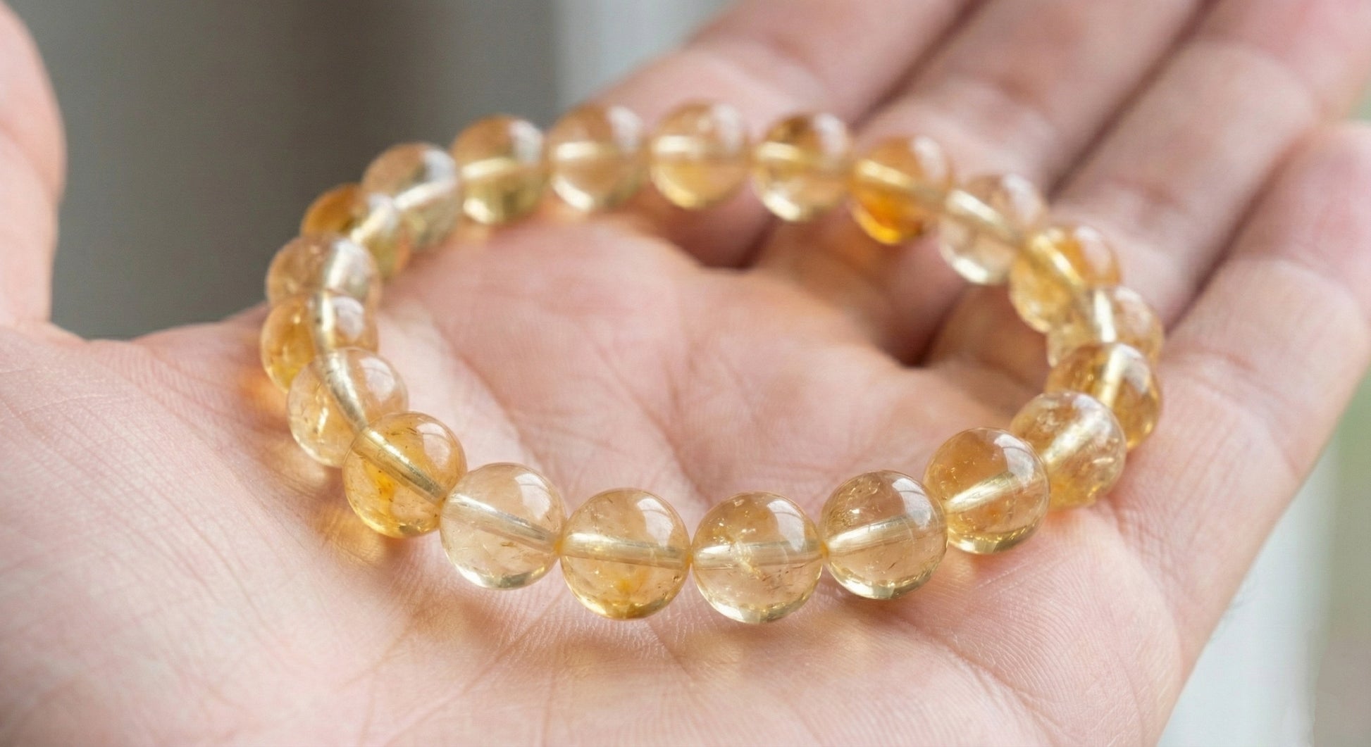 Hand holding a round citrine gemstone beaded bracelet with translucent yellow beads