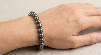 Hand wearing a polished black hematite bead bracelet on a neutral fabric surface