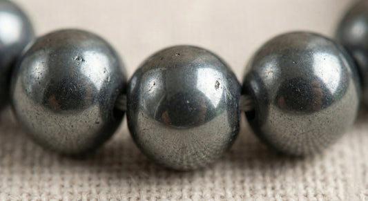 Close-up of a hematite bead necklace with metallic textured surface on woven fabric