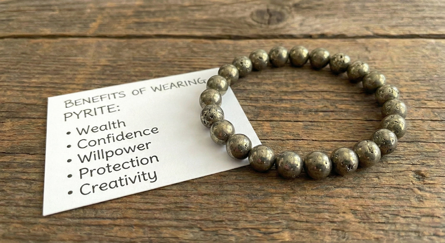 Pyrite beaded bracelet on wooden surface with note listing benefits including wealth, confidence, and creativity