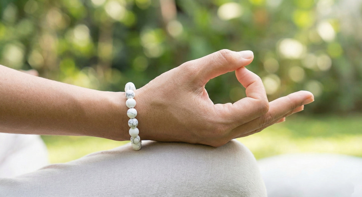Close-up of a hand in meditation pose wearing a white beaded bracelet with blurred greenery background