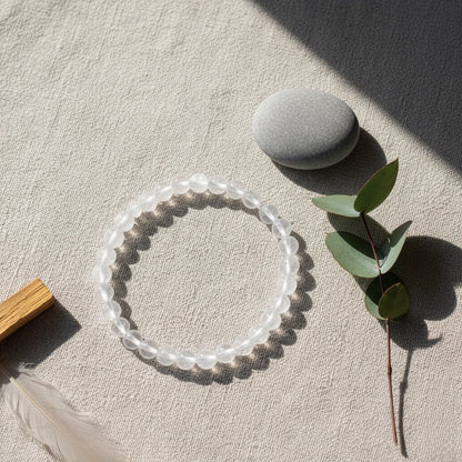 Clear round beaded bracelet on beige fabric with smooth gray stone and eucalyptus branch