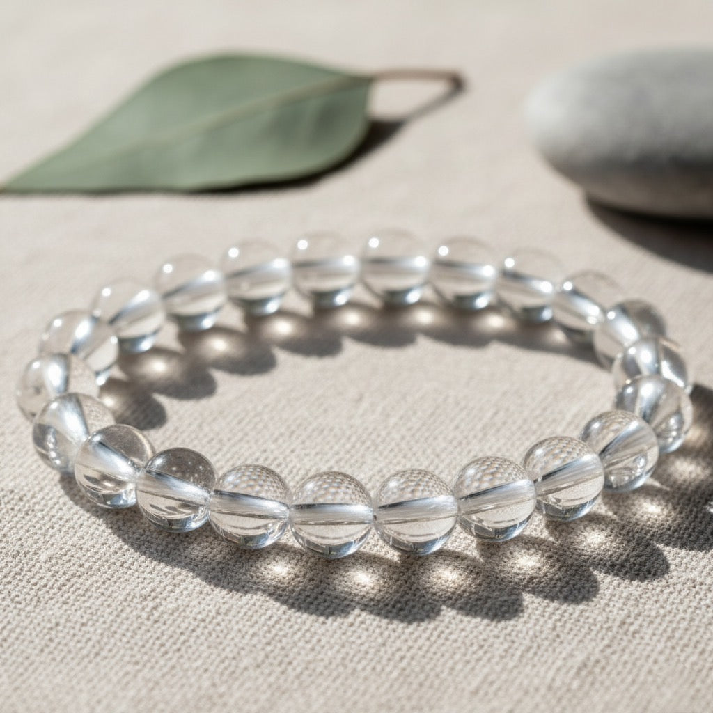 Clear round crystal bead bracelet on beige fabric with green leaf and smooth stone background