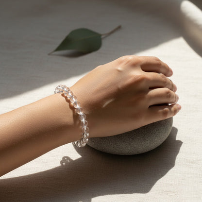 Close-up of hand wearing a clear beaded bracelet resting on a smooth gray stone on fabric