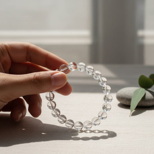 Hand holding clear quartz crystal bead bracelet with natural stones and green leaves on linen surface