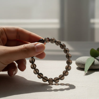 Hand holding a smoky quartz bead bracelet with smooth stones and a eucalyptus branch in soft natural light