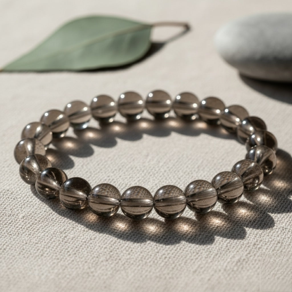 Smoky quartz beaded bracelet on beige fabric with leaf and stone in soft natural light