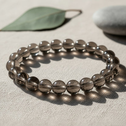 Smoky quartz beaded bracelet on beige fabric with leaf and stone in soft natural light