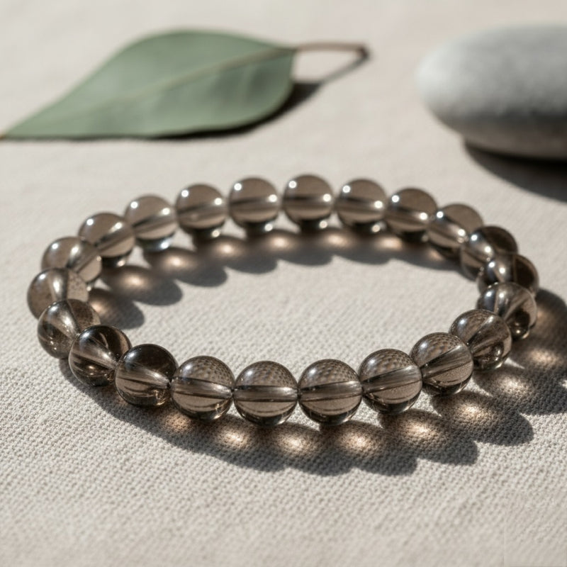 Smoky quartz beaded bracelet on beige fabric with leaf and stone in soft natural light