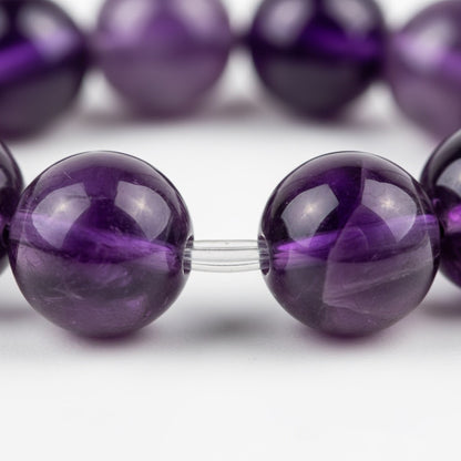 Close-up of polished purple amethyst gemstone beads strung on clear elastic cord