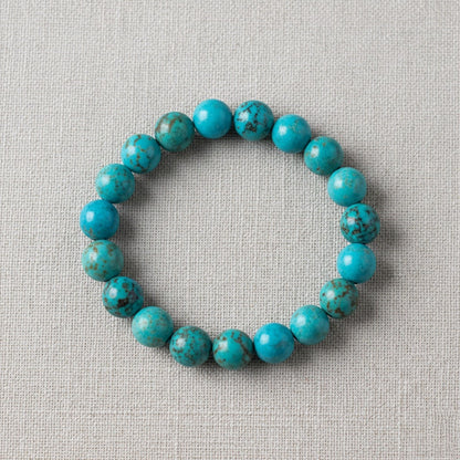Round turquoise bead bracelet with natural brown veining on beige fabric background
