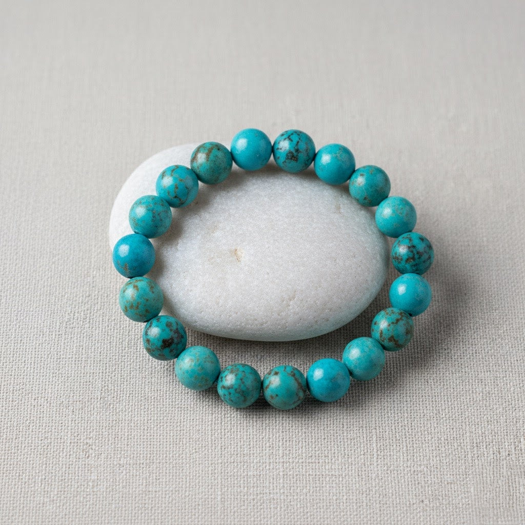 Turquoise beaded bracelet arranged around smooth white stone on beige fabric
