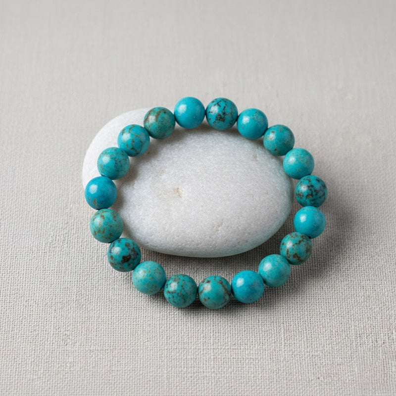 Turquoise beaded bracelet arranged around smooth white stone on beige fabric